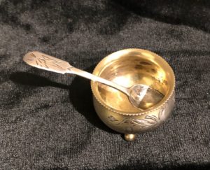 Солонка на трёх круглых ножках. Серебро, литьё, золочение, гравировка, (есть место для монограммы). 1908-1917 гг., «84» проба с головой в кокошнике повернутой влево, клеймо мастера «ИС», переклеймение советского времени. Вес 23, 5 гр. высота 2,7 см., диаметр 4 см., Ложечка. Длинна 7,8 см., вес 6 гр., Серебро, литьё, гравировка. Клейма: «84» проба с гербом Москвы, клеймо мастера «КЛ».